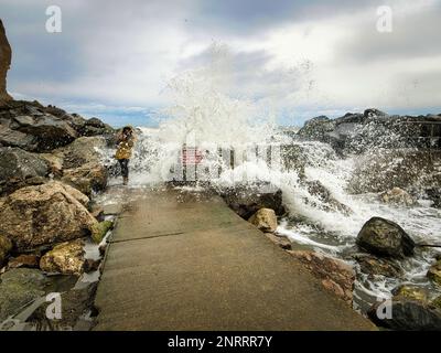 Der Sturm Otto geht im Gefolge über stürmische Meere und dramatische Wellen, die sowohl das Wellenbrecherwasser bei Staithes als auch einen unachtsamen Zuschauer treffen. Stockfoto