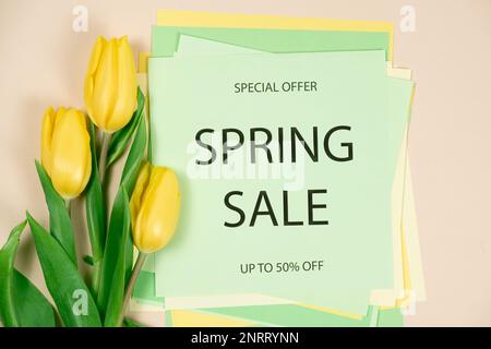 Frühlingsangebot - Sonderangebot bis zu 50 % Rabatt, gelbe Tulpen auf beigefarbenem Hintergrund, Text auf hellgrünem Hintergrund Stockfoto