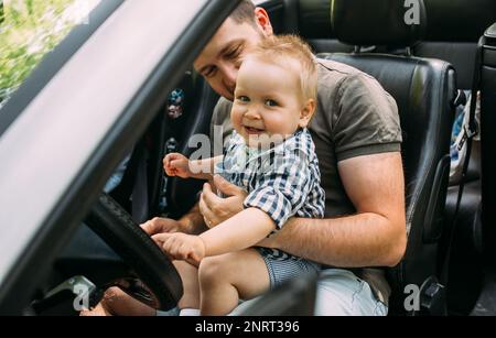 Papa zeigt seinem kleinen Sohn, wie er das Auto fährt, während er hinter dem Steuer sitzt Stockfoto