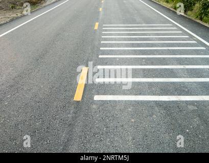 Die weißen Querstreifenstreifen auf der Asphaltstraße verursachen ein lautes Geräusch, das den Fahrer darauf aufmerksam macht, bevor er die Kreuzung in der Straße erreicht Stockfoto