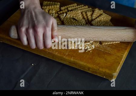 Hände, die Kekse mit einer Walznadel zerbrechen, um die knusprige Basis eines Käsekuchen zuzubereiten Stockfoto