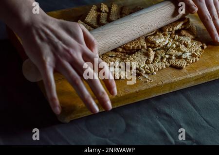 Hände, die Kekse mit einer Walznadel zerbrechen, um die knusprige Basis eines Käsekuchen zuzubereiten Stockfoto