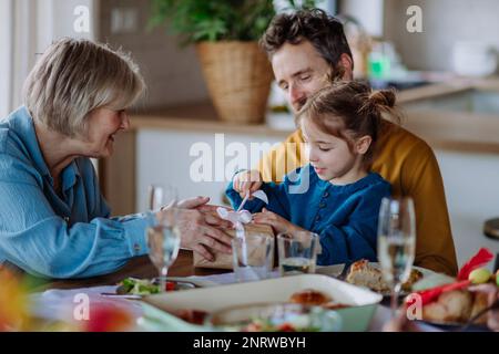 Ein kleines Mädchen, das beim Familienessen ein Geschenk auspackt. Stockfoto