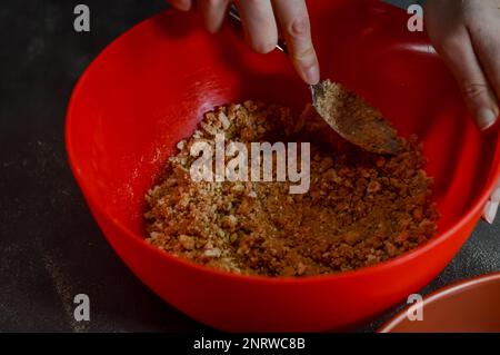 Die Hände mischen Kekskrümel, geschmolzene Butter und Zucker in einer Schüssel, um die Basis eines Käsekuchen zu bilden Stockfoto