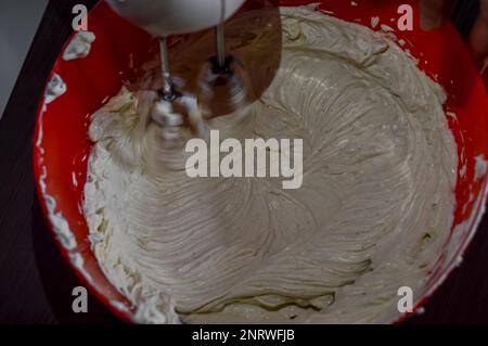 Mixer mischt frischen Weißkäse und Eier zu Käsekuchen-Sahne Stockfoto