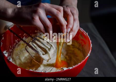 Die Hände geben Ei zu frischem Weißkäse, der zu Käsekuchen-Creme zusammengeschlagen wird Stockfoto