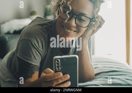 Fröhliche, moderne junge Frau lächelt und telefoniert mit dem Mobiltelefon. Technologie Online-Smartphone-App und Menschen. Weiblich mit Brille, die auf Cel liest Stockfoto