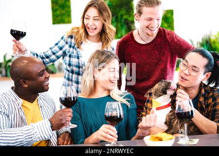 Trendige Menschen, die Rotwein auf Dinnerparty-Stimmung anstoßen - multirassische Freunde, die gemeinsam mit dem Hund Spaß haben bei der Happy Hour am Restaurant des Weinguts Stockfoto