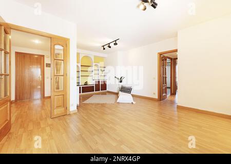 Wohnzimmer eines leeren Hauses mit doppelten hölzernen Zugangstüren, einem eingebauten Bücherregal mit Gipsregalen und Holzschubladen und Eichenboden Stockfoto