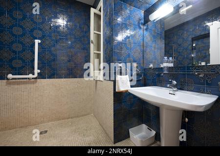 Antikes Bad mit Dusche im bulgarischen Stil mit gefliestem Fußboden und Halbwand, blauen Fliesen im Vintage-Stil und weißem Porzellanwaschbecken mit Spiegel Stockfoto