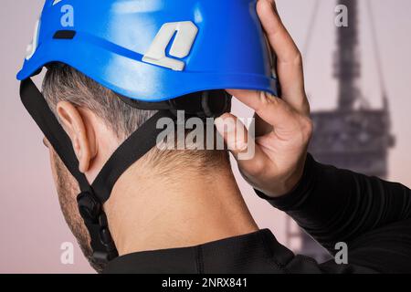 Mann, Turmarbeiter. Arbeiten in der Höhe. Radioantenne. Er setzt einen Helm auf, einen Schutzhelm. Passt den Helm an. Stockfoto