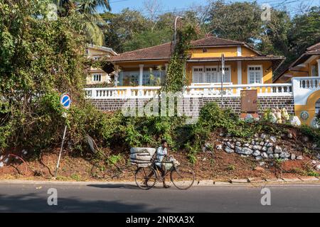 Panjim, Goa, Indien - Januar 2023: Ein indischer Mann, der mit seinem Fahrrad an einem alten großen portugiesischen Haus in der Altinho-Gegend von Panaji vorbeiläuft. Stockfoto