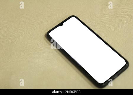Ein schwarzes Mobiltelefon mit einem leeren weißen Bildschirm befindet sich auf einer Bank, die mit einem strukturierten Tuch gepolstert ist. Geeignet für Handy- oder Gadget-Modelle Stockfoto