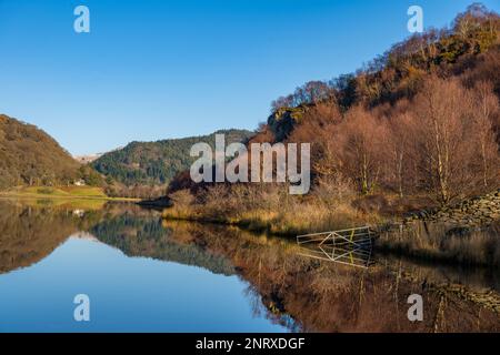 Blick nach Norden über Llyn Dinas, in der Nähe von Beddgelert, Nordwales in Richtung Bäume und Hügel von Snowdonia. An einem sonnigen Wintertag. Stockfoto