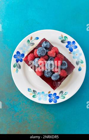 Ein Stück Kuchen mit Mohnsamen und Beerengelee, Kuchen auf einem Teller, der mit saftigen Himbeeren und Heidelbeeren verziert ist Stockfoto