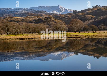 Blick nach Osten über Llyn Dinas, in der Nähe von Beddgelert, Nordwales in Richtung Bäume und Hügel von Süd-Snowdonia. An einem sonnigen Wintertag. Stockfoto