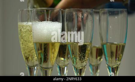 Ich gieße Champagner ein. Gieße den Champagner in viele Gläser. Der Barkeeper schüttet Champagner in die Glasnaht. Blasen und Schaum steigen im Trinkglas auf Stockfoto