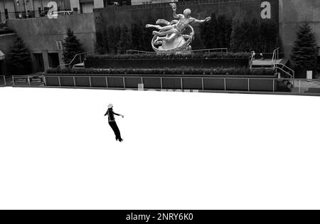 Eisläufer und die 1934 vergoldete Bronzeskulptur von Prometheus von Paul Manship auf der Eisbahn des Rockefeller Center in New York City, NY Stockfoto