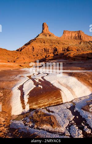 Kalium- und Salzkristalle bilden sich entlang des Randes eines Mineral Seep bei Moab, Utah, mit einem Wingate Sandstein butte dahinter. Stockfoto