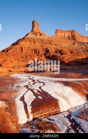 Kalium- und Salzkristalle bilden sich entlang des Randes eines Mineral Seep bei Moab, Utah, mit einem Wingate Sandstein butte dahinter. Stockfoto