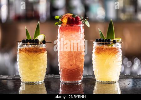 Mai Tai Cocktails in hawaiianischen Gläsern garniert mit Ananas, Blaubeeren und Erdbeeren an der Bar. Stockfoto