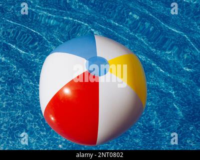 Aufblasbarer Strandball schwimmt in klarem blauem Wasser oder im Außenpool Stockfoto