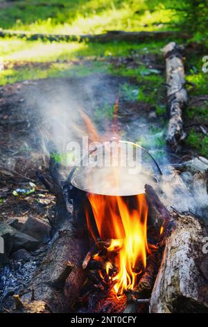 Touristischer Bowler mit Essen am Lagerfeuer, Kochen bei der Wanderung, Camping-Aktivitäten im Freien. Zubereitung von Pilaf oder Suppe auf Feuer. Authentische Abenteuer und Stockfoto