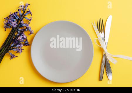 Frühlingstisch mit grauer Platte und blauen Hyazinthen-Blüten auf gelbem Hintergrund. Draufsicht, flach liegend, Kopierbereich. Stockfoto
