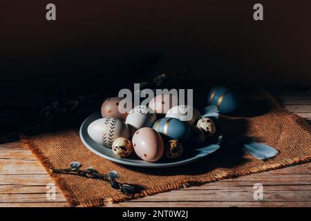 Teller mit bemalten Ostereiern und Weidenzweigen auf einem Holztisch. Ostergrußkarte. Nahaufnahme. Stockfoto
