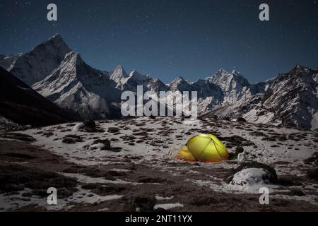 Konzept des extremen Campings im Freien. Nachts Camping im Winter in den Bergen. Einsames Zelt beleuchtet von innen im Tal unter dem Berg Ama Dablam auf einem Stockfoto