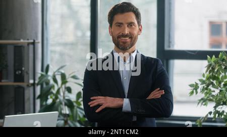 Erfolgreicher, lächelnder, erwachsener Geschäftsmann, steht im Amt mit überkreuzten Armen, selbstbewusster Geschäftsführer, CEO-Experte des Unternehmens Stockfoto