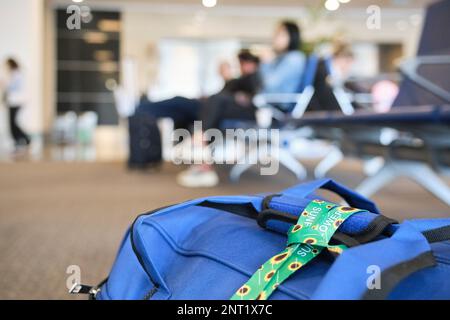 Eine Trageschlaufe mit Sonnenblumen, ein Symbol für Menschen mit unsichtbaren oder versteckten Behinderungen, die an eine Reisetasche auf dem Boden eines Flughafens gebunden ist. Stockfoto