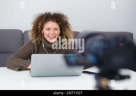 Fröhlicher Influencer filmt Video-Blog zu Hause. Glückliche junge Frau, die mit einem Lächeln auf dem Camcorder spricht Stockfoto