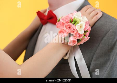 Junge Frau mit Ansteckblume umarmt ihre Abschlussball-Verabredung auf gelbem Hintergrund, Nahaufnahme Stockfoto