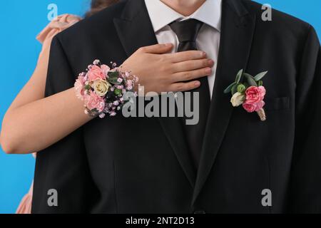 Junge Frau mit Ansteckblume umarmt ihre Abschlussball-Verabredung auf blauem Hintergrund, Nahaufnahme Stockfoto