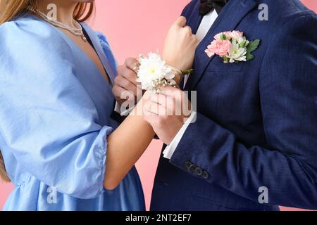 Ein Junge, der sein Date-Handgelenk mit Ansteckblume vor pinkfarbenem Hintergrund aufsetzt, Nahaufnahme Stockfoto