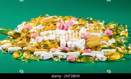 Ein Haufen mehrfarbiger Pillen und Kapseln mit Bioadditiven mit Reflexion auf grünem Hintergrund Stockfoto