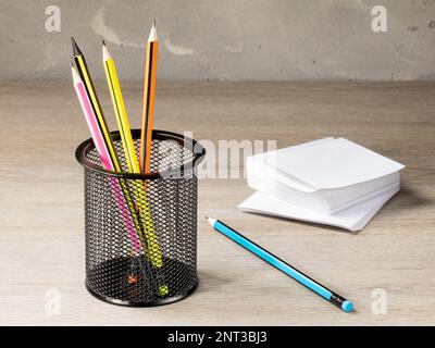 Büromaschinenbehälter aus Netzgewebe mit Bleistiften und einem Stapel Papier für Notizen auf dem Hintergrund des Bürotischs. Stockfoto