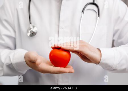Ein Arzt in weißem Kittel, der ein rotes Herz in den Händen hält. Medizinisches Versorgungskonzept und Ärztedienstkonzept. Stockfoto