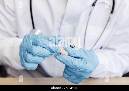 Ein HNO-Arzt hält ein Hörgerät in den Händen. Der Arzt konsultiert den Patienten. Stockfoto