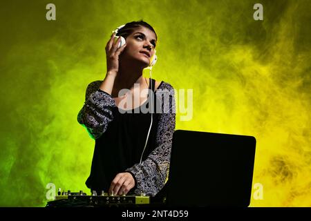 DJ-Mädchen, die Musik auf einem Mixer spielt. Gelber und grüner Rauch im Hintergrund Stockfoto