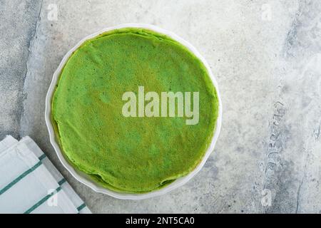 Grüne Pfannkuchen. Runde, dünne, grüne Spinat-Crepe-Pfannkuchen mit rotem und schwarzem Kaviar und Joghurt-Sauce auf grauem Betonhintergrund. Gesundes veganes Frühstück Stockfoto