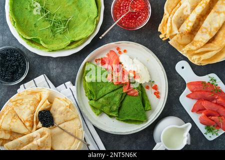 Verschiedene grüne und weiße Pfannkuchen. Dünner grüner Spinat und weiße Crepe-Pfannkuchen mit rotem und schwarzem Kaviar, Sauce auf grauem Beton-Tischbrea Stockfoto