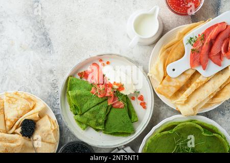 Verschiedene grüne und weiße Pfannkuchen. Dünner grüner Spinat und weiße Crepe-Pfannkuchen mit rotem und schwarzem Kaviar, Sauce auf grauem Beton-Tischbrea Stockfoto