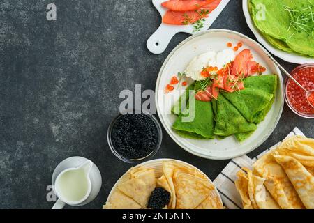 Verschiedene grüne und weiße Pfannkuchen. Dünner grüner Spinat und weiße Crepe-Pfannkuchen mit rotem und schwarzem Kaviar, Sauce auf grauem Beton-Tischbrea Stockfoto