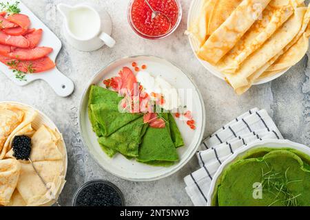 Verschiedene grüne und weiße Pfannkuchen. Dünner grüner Spinat und weiße Crepe-Pfannkuchen mit rotem und schwarzem Kaviar, Sauce auf grauem Beton-Tischbrea Stockfoto