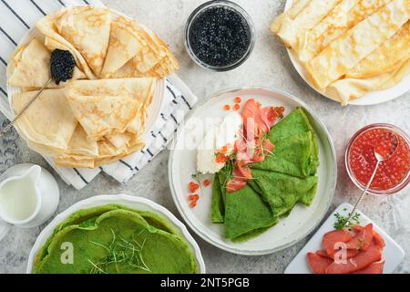 Verschiedene grüne und weiße Pfannkuchen. Dünner grüner Spinat und weiße Crepe-Pfannkuchen mit rotem und schwarzem Kaviar, Sauce auf grauem Beton-Tischbrea Stockfoto