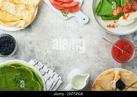 Verschiedene grüne und weiße Pfannkuchen. Dünner grüner Spinat und weiße Crepe-Pfannkuchen mit rotem und schwarzem Kaviar, Sauce auf grauem Beton-Tischbrea Stockfoto