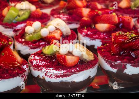 Ein großer Haufen köstlicher Desserts mit Schokoladencreme und Joghurt, dekoriert mit Scheiben von frischer Erdbeer-Banane und Kiwi in Patisserie Stockfoto
