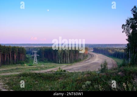 Der Endanker unterstützt Überlandleitungen mit Drähten am Horizont, an einem wunderschönen Abhang des farbenfrohen orangefarbenen Sonnenuntergangs über dunklem Wald, durch den Stockfoto